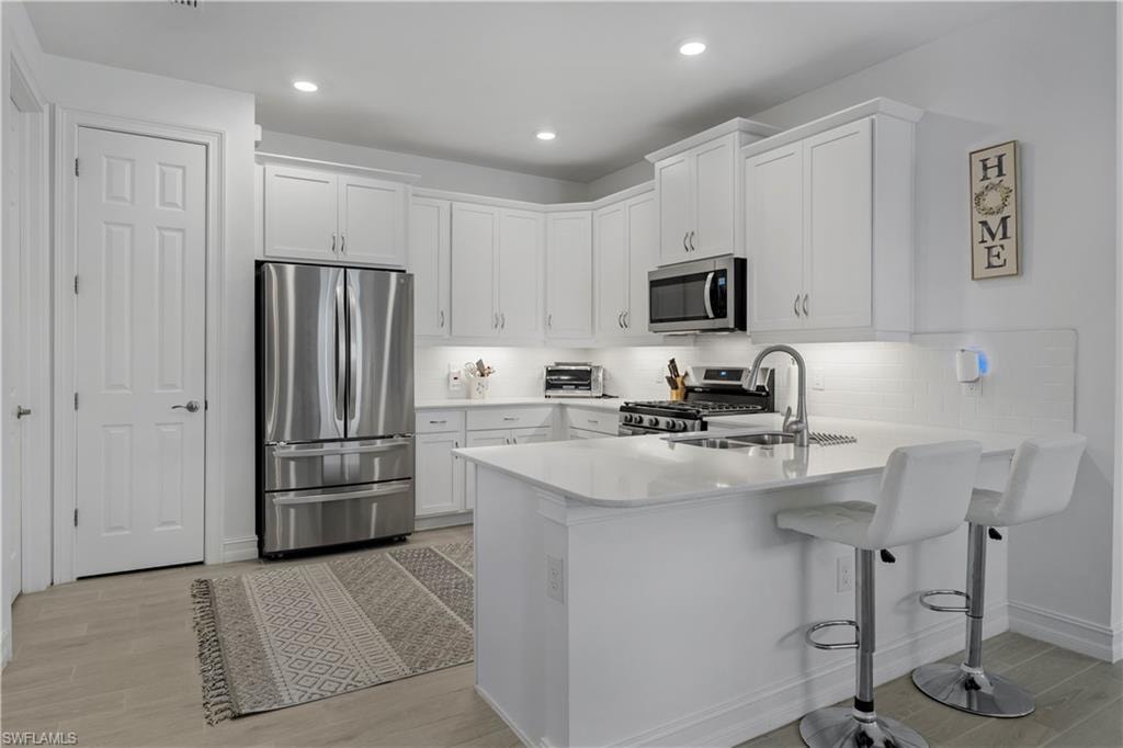 Kitchen featuring white cabinetry, stainless steel appliances, white countertop island with sink, and light wood-finish flooring