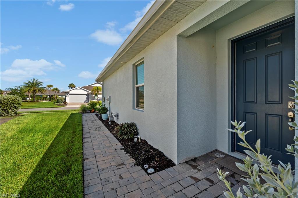 Stucco exterior with a paneled entry door, paver walkway, and well-maintained landscaping