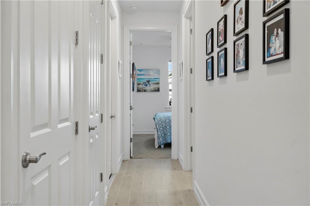 Hallway featuring light wood-finish flooring, white paneled doors with brushed nickel hardware, and neutral wall tones