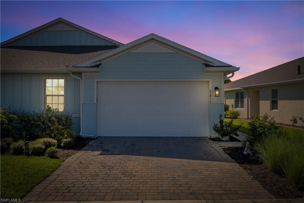 Light blue exterior siding, white trim accents, prominent garage, exterior wall lantern, and paver driveway