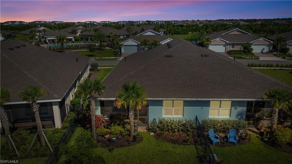 Elegant single-story residence featuring a dark architectural shingle roof, large picture windows with yellow-toned frames, and mature landscaping including palm trees and established plantings