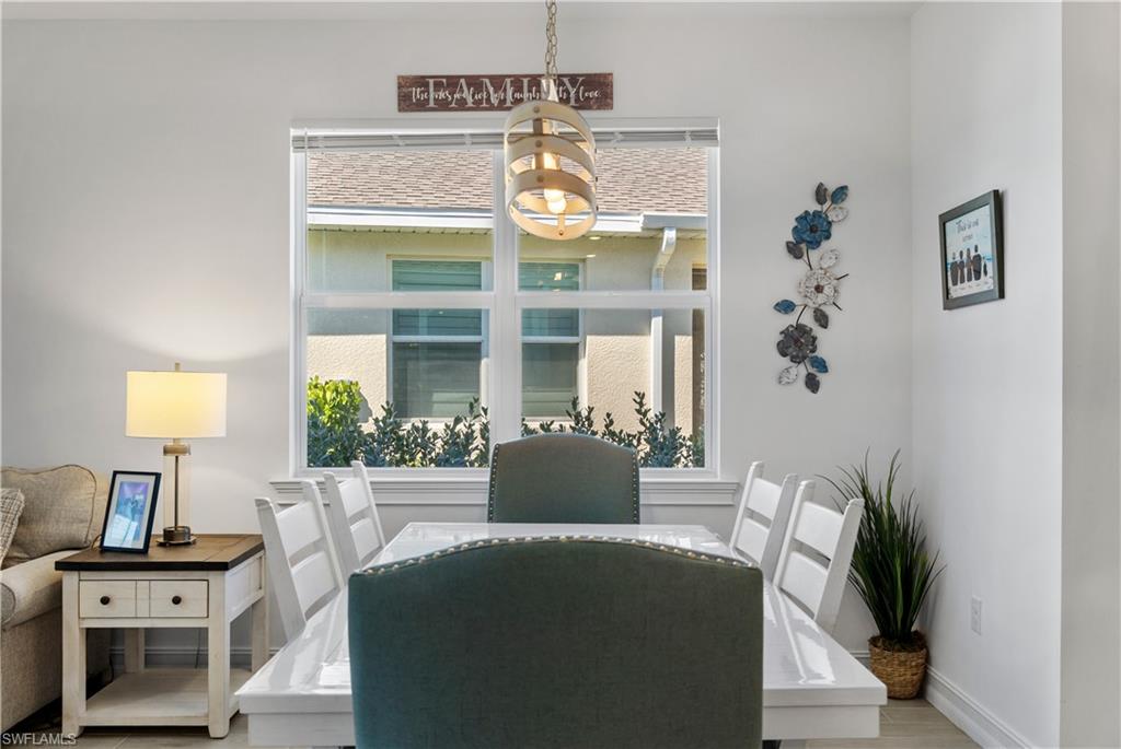Bright dining space anchored by a large round table with seating for six, featuring white shaker-style chairs and a pendant light fixture