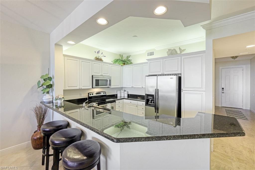 Kitchen with recessed lighting, dark stone counters, appliances with stainless steel finishes, a breakfast bar area, and a peninsula