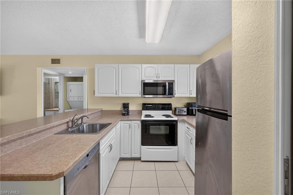 Kitchen featuring white cabinetry, a stainless steel refrigerator, a built-in microwave, and a double basin sink