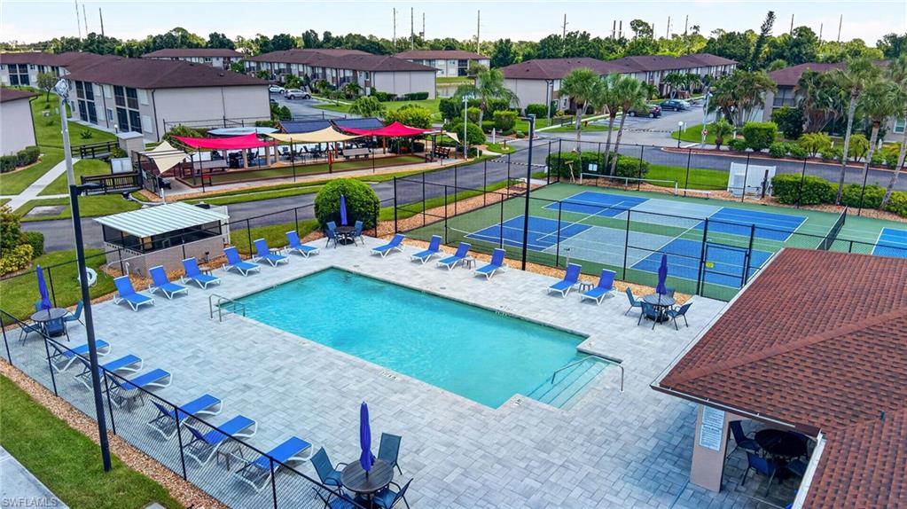 Rectangular swimming pool with paver decking, multiple pickleball courts, covered outdoor seating areas, and a dedicated pool house