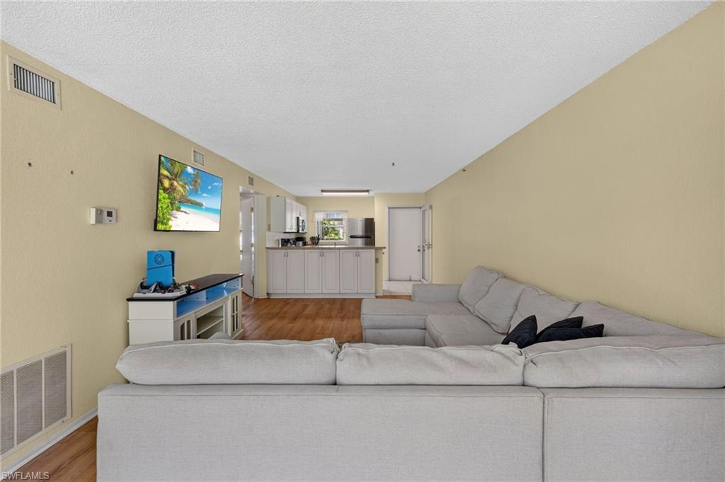 Integrated living and kitchen area featuring wood-finish flooring, white cabinetry, and light-toned walls
