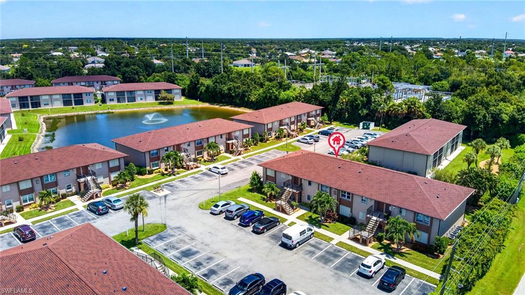Multiple residential buildings featuring brown roofs, an artificial pond with a fountain, and paved parking areas