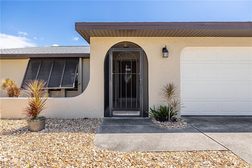 Arched entry with security screen door, attached single-car garage, exterior wall lantern, and gravel landscaping
