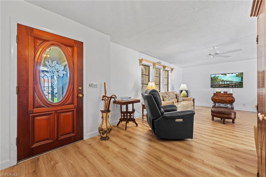 Wood-finish flooring throughout, solid wood entry door with oval glass insert, white walls, and a ceiling fan with integrated lighting