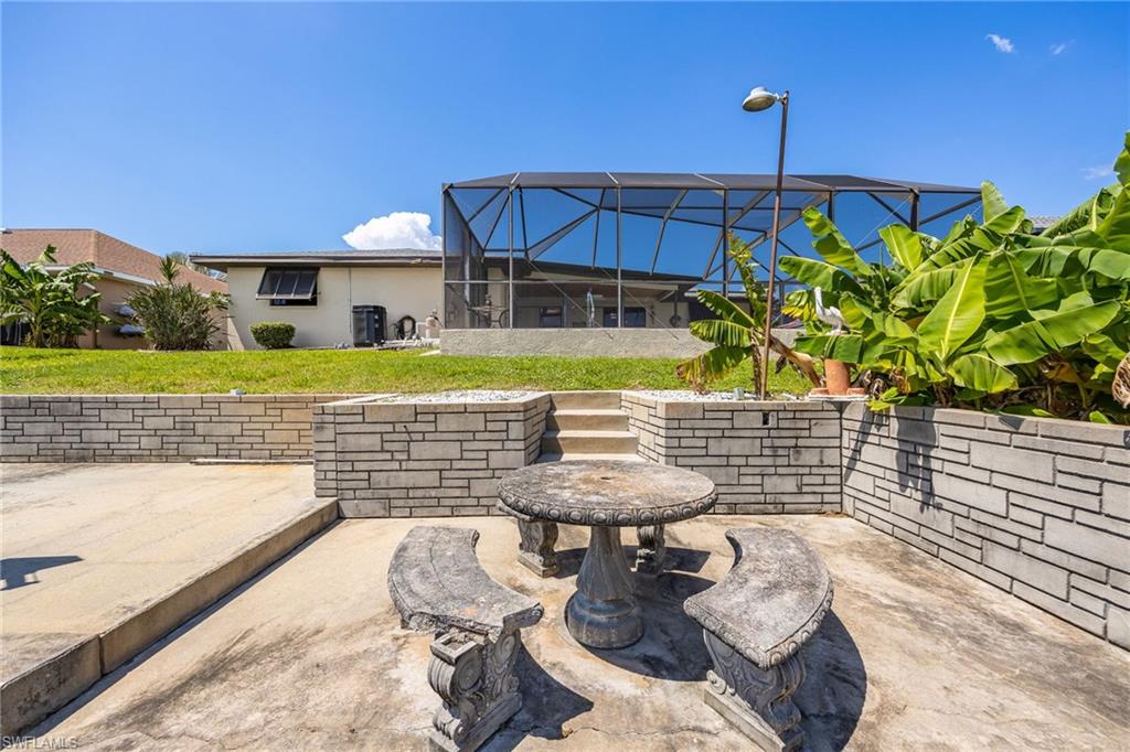 Screened-in pool enclosure, concrete patio, stone retaining walls, stone steps, and mature tropical foliage