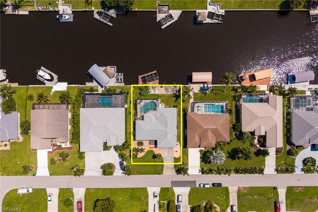 Waterfront property featuring a private boat dock, in-ground swimming pool, concrete driveway, and mature landscaping