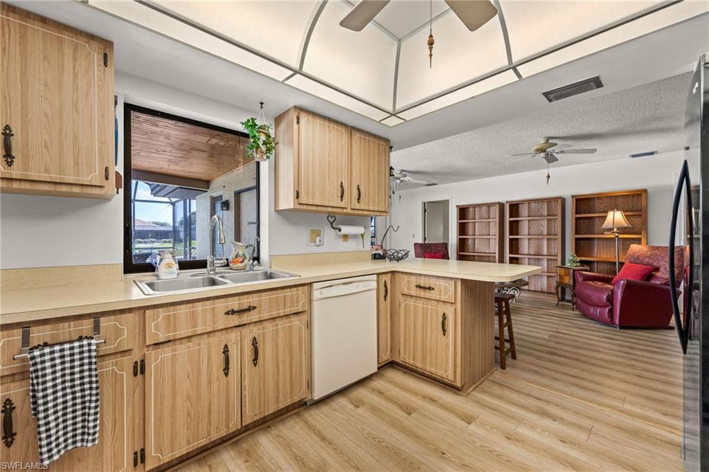 Kitchen featuring wood-finish cabinetry, a double basin stainless steel sink, beige countertops, and a built-in dishwasher