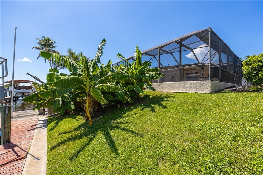 Screened-in outdoor living space with a concrete patio, bordered by a sloped lawn and lush plantings