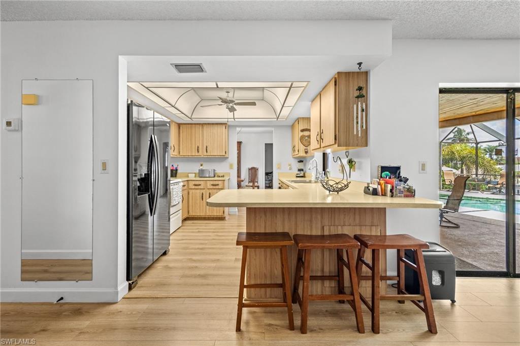 Kitchen featuring wood-finish flooring, light wood cabinetry, a stainless steel refrigerator, and a breakfast bar