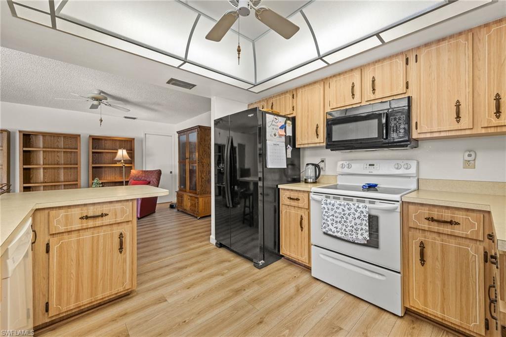Kitchen featuring wood-finish cabinetry, light-toned countertops, and a full suite of appliances including a black refrigerator, white range, and black microwave