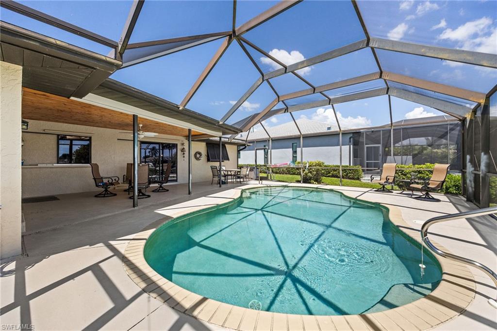 Screened enclosure with an in-ground swimming pool, concrete pool deck, and a covered patio featuring a wood-finish ceiling