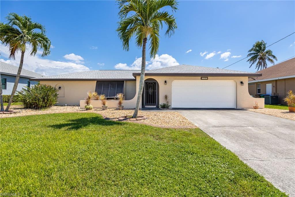 Single-story residence featuring a two-car garage, concrete driveway, and mature landscaping with palm trees