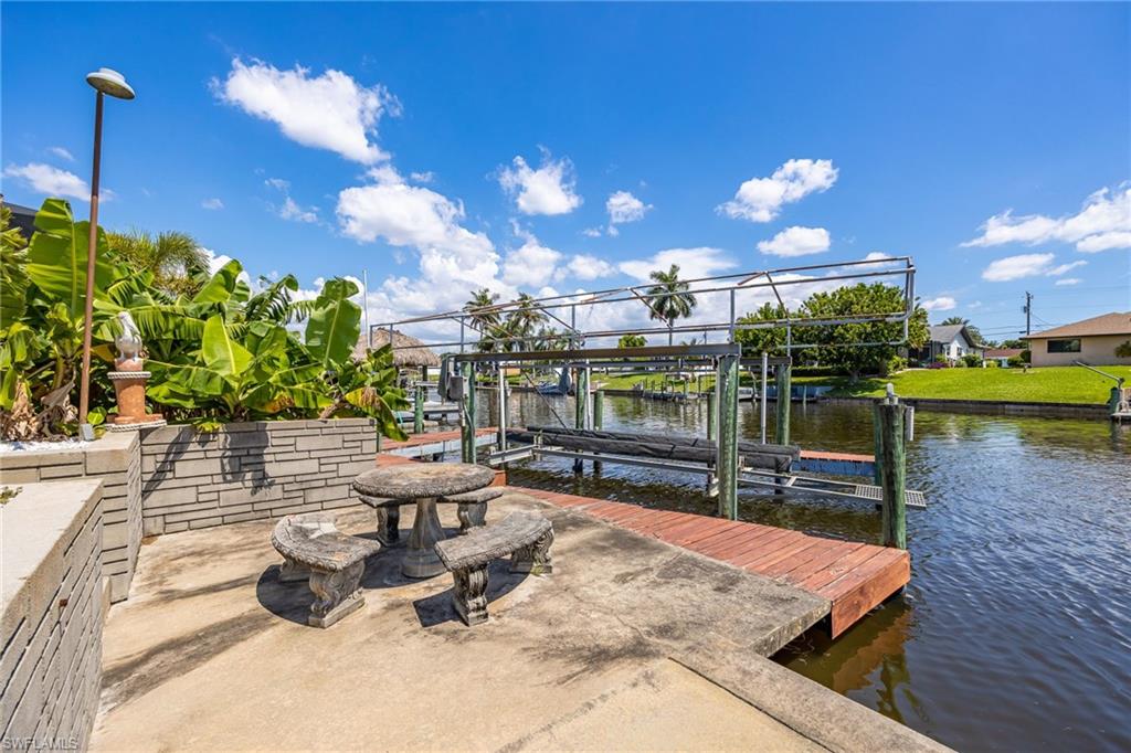 Concrete patio with a stone-finish table and benches, canal-front wood dock, and boat lift