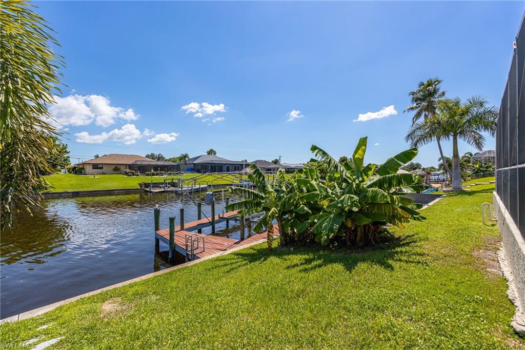 Waterfront property featuring a private boat dock, lush green lawn, and mature palm trees