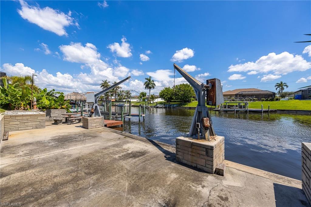 Waterfront property with concrete dock, dual boat lifts, and mature tropical landscaping