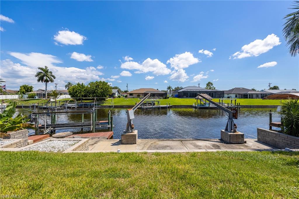 Waterfront property with boat lift, concrete boat ramp, and manicured lawn