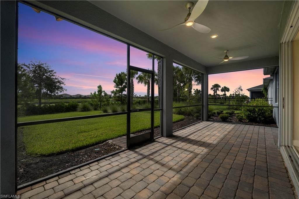 Screened lanai featuring paver flooring, overhead lighting, two ceiling fans, and a distant landscape with palm trees