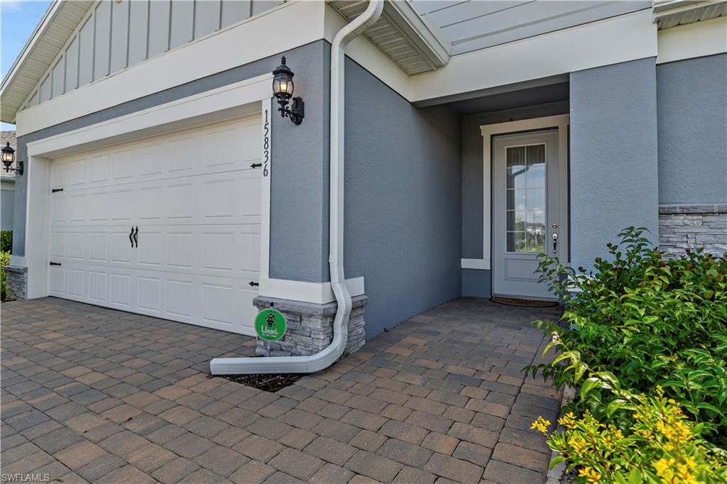 Paver driveway, stone veneer accents, recessed entry, overhead garage lighting, and decorative garage door hardware
