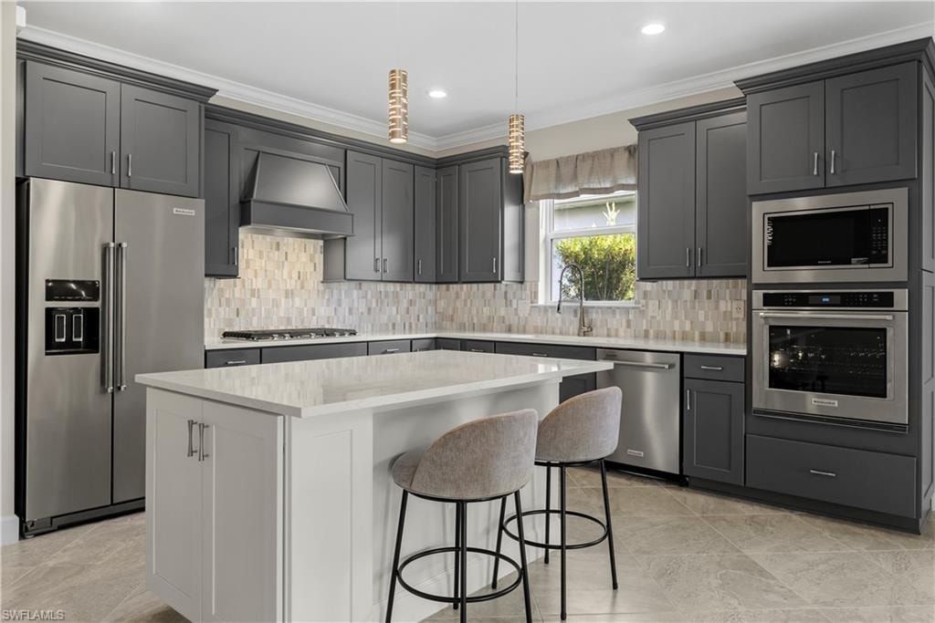 Kitchen featuring shaker-style cabinetry, stainless steel appliances, a center island with a light-toned countertop, and a tiled backsplash