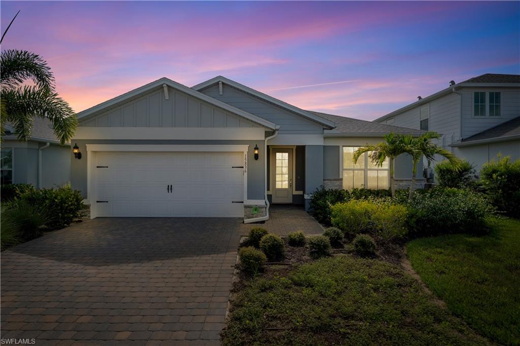 Single-story residence featuring a two-car garage with carriage-style doors, a paver driveway, an inviting entryway with a glass-paneled door, and curated landscaping