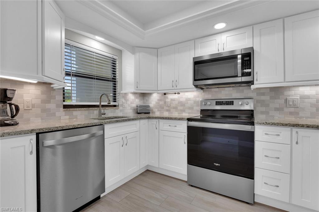 White shaker cabinetry, stainless steel appliances, mosaic tile backsplash, light-toned countertop, and wood-finish flooring