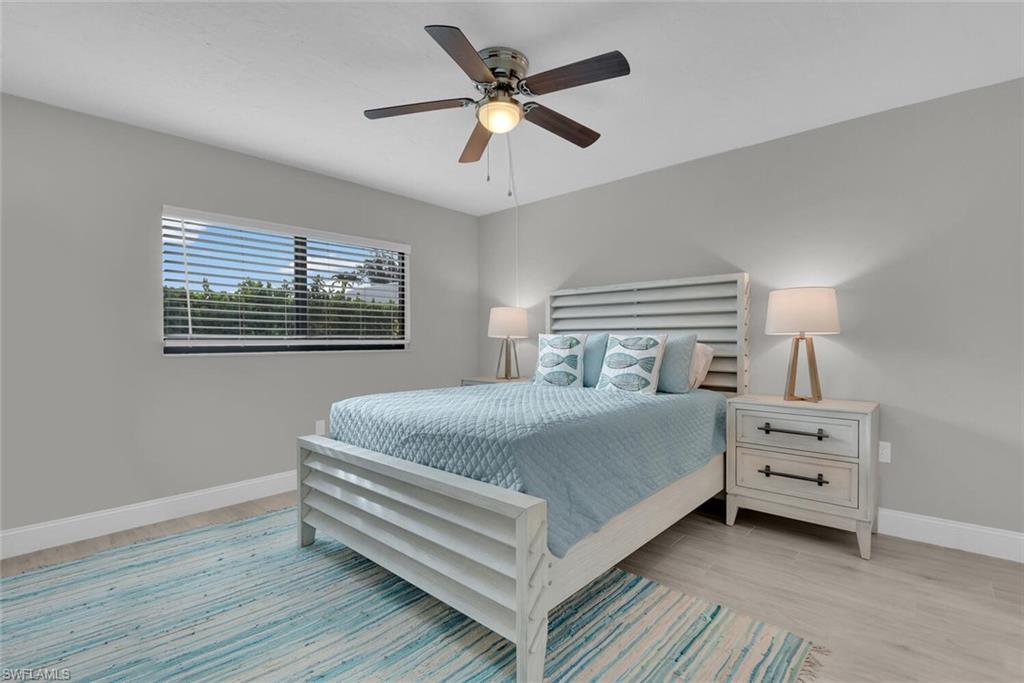 Light gray wall paint, wood-finish flooring, window with horizontal blinds, ceiling fan with integrated lighting, and white wood-slat headboard