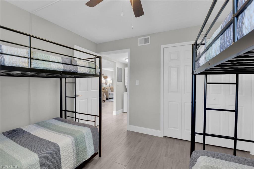Room featuring two bunk beds, wood-finish flooring, a ceiling fan, and white bi-fold closet doors