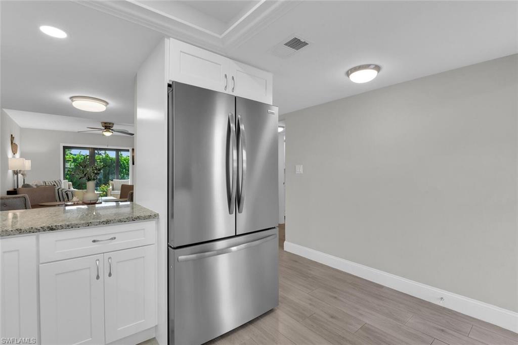 Stainless steel French door refrigerator, white shaker-style cabinetry, light-toned wood-finish flooring, and a stone-finish countertop