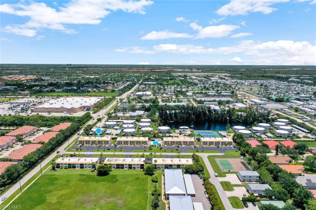 Aerial perspective showcasing community grounds with a pond, tennis courts, and multi-unit residential buildings