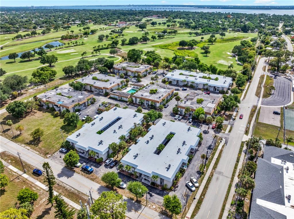 Aerial perspective showcasing multiple residential buildings, a golf course with water features, a prominent roadway, and a distant body of water