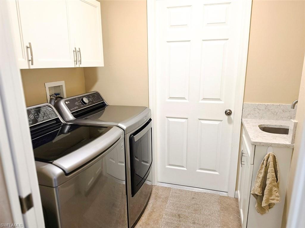 Laundry area featuring white cabinetry with silver hardware, a built-in sink with stone-finish countertop, and tile flooring