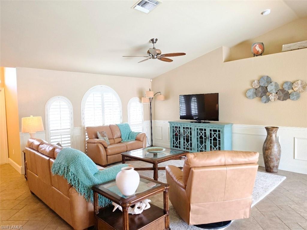 Vaulted ceiling with a ceiling fan, white arched windows, lower wall paneling, and an upper wall shelf