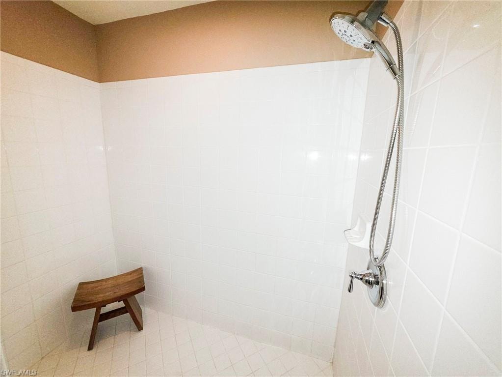 White tile shower enclosure with a handheld shower head and an adjustable wall-mounted shower fixture