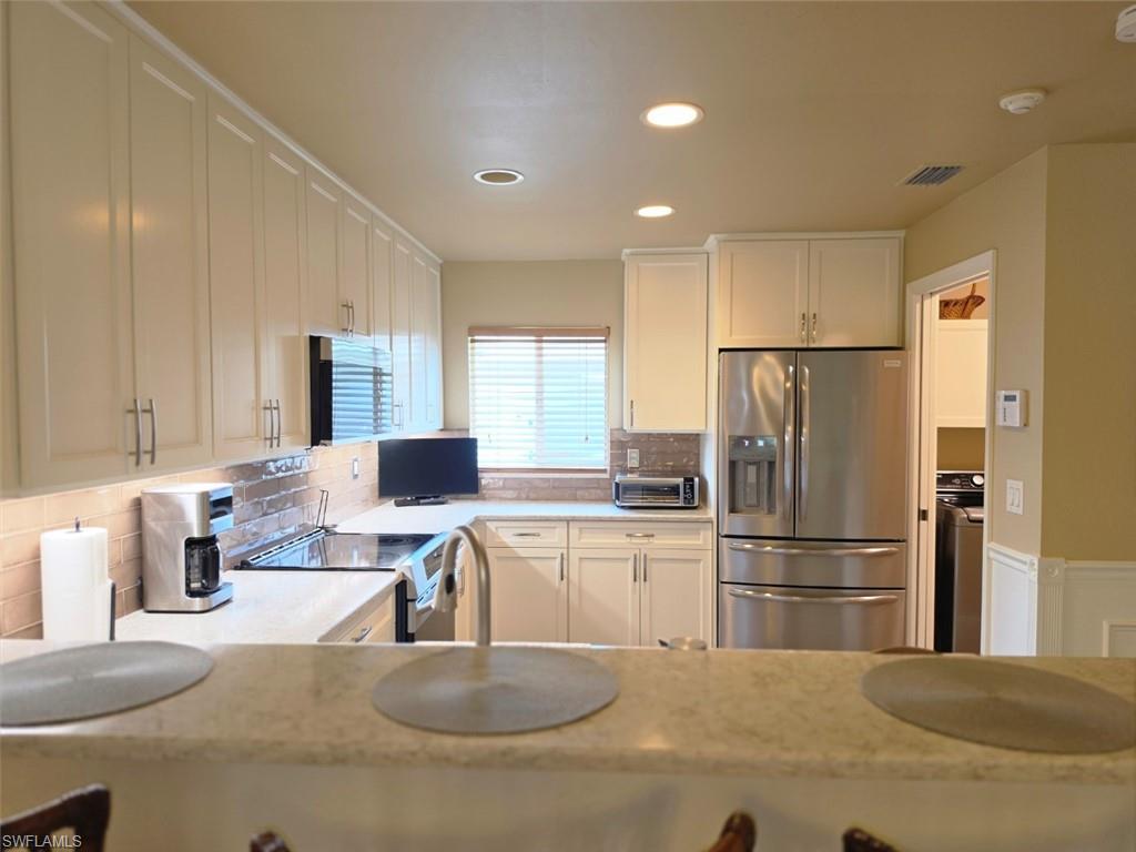 Kitchen featuring extensive cabinetry, undermount sink with a gooseneck faucet, integrated stainless steel appliances, recessed lighting, and a tiled backsplash