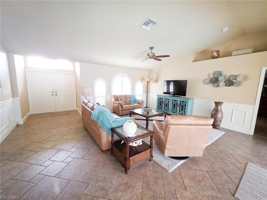 Vaulted ceiling, ceiling fan, arched windows, wainscoting, and tile flooring