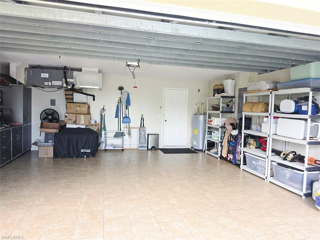 Spacious garage with light-toned tiled flooring, exposed ceiling joists, built-in cabinetry, and a water heater
