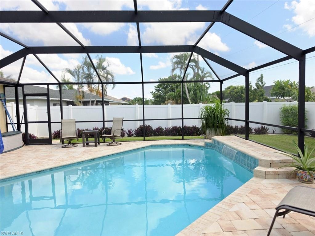 Screened outdoor pool area featuring a paved deck, an integrated water feature, and a privacy fence