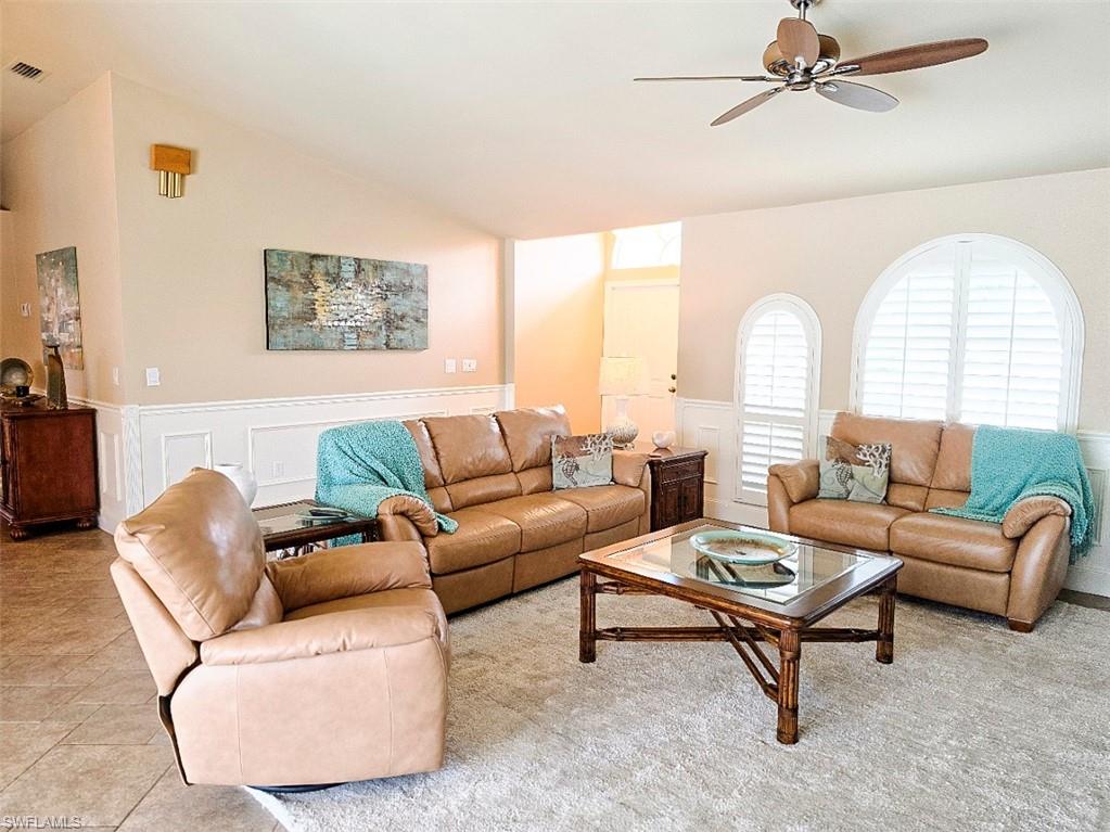 Vaulted ceiling with a ceiling fan, arched windows with plantation shutters, wainscoting, and tile flooring