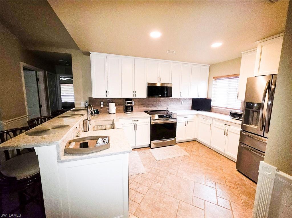 U-shaped kitchen with white cabinetry, stainless steel appliances, a breakfast bar, and tile flooring