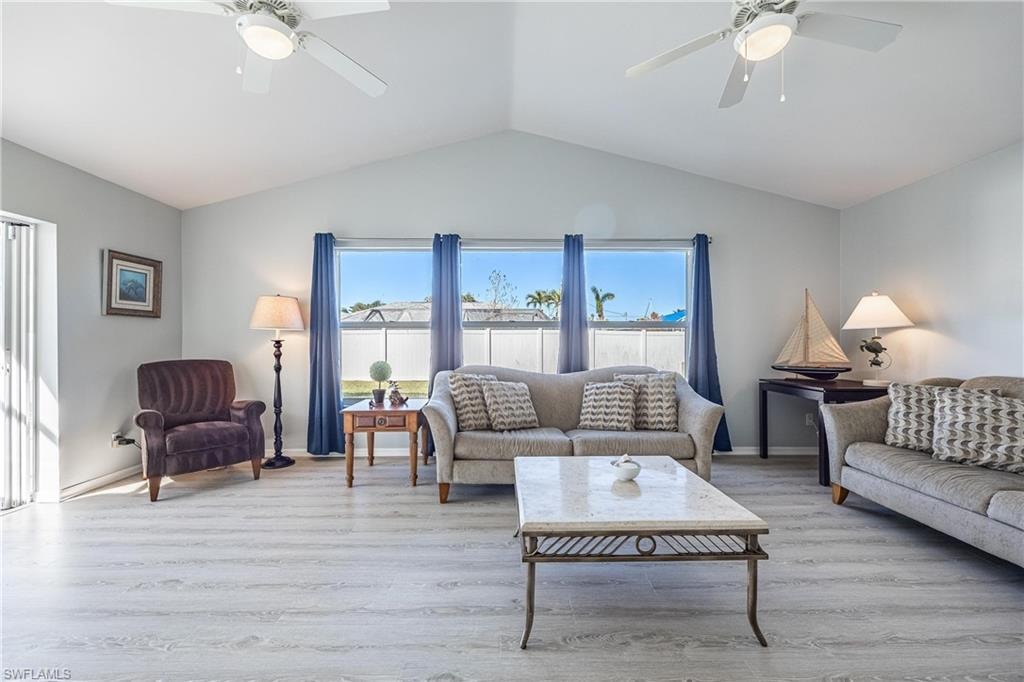 Living room with ceiling fan, vaulted ceiling, baseboards, and light wood-type flooring