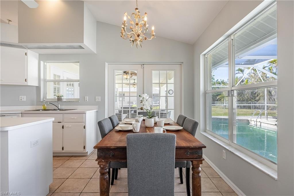 Dining area with ceiling fan with notable chandelier, vaulted ceiling, and light tile patterned floors