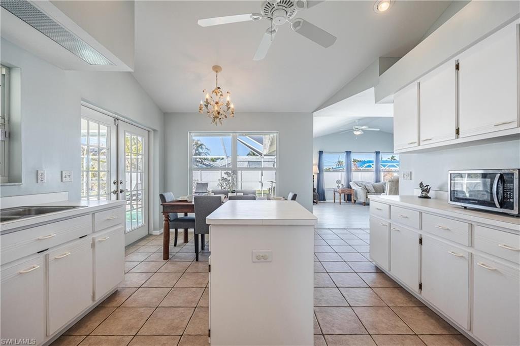 Kitchen featuring lofted ceiling, stainless steel microwave, a kitchen island, white cabinetry, and ceiling fan with notable chandelier