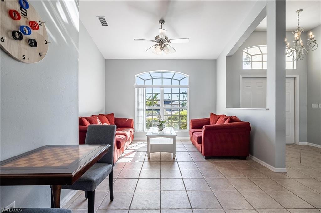 Living room featuring lofted ceiling, visible vents, light tile patterned flooring, baseboards, and ceiling fan with notable chandelier