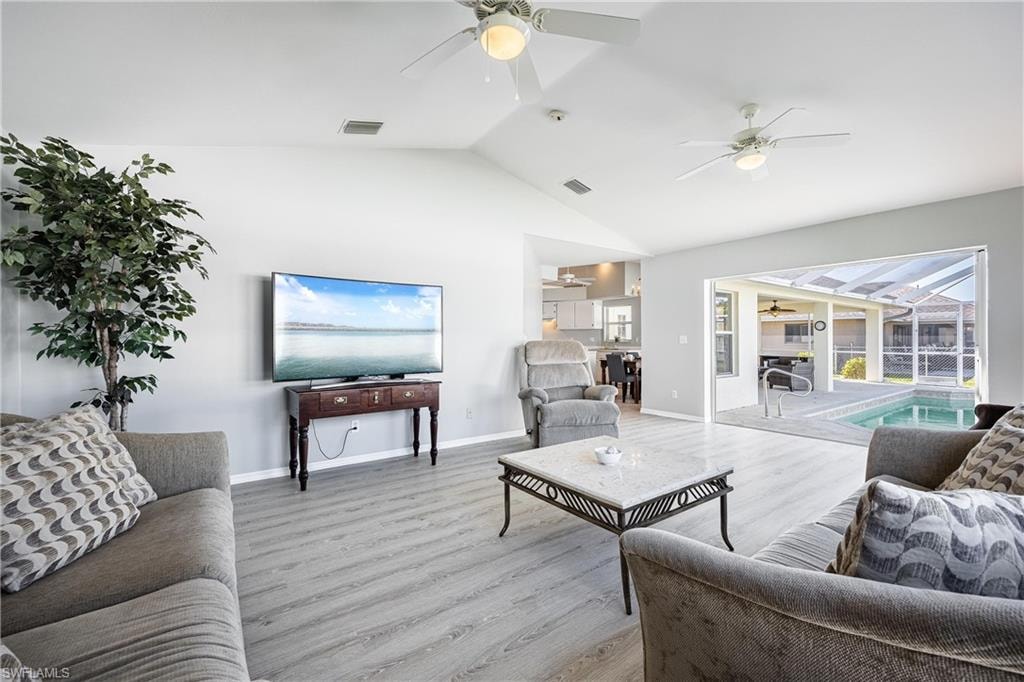 Living room with lofted ceiling, visible vents, light wood finished floors, and ceiling fan