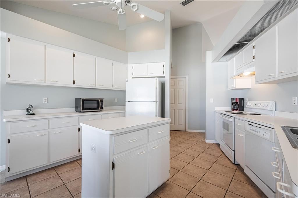 Kitchen with light tile patterned flooring, white appliances, ceiling fan, under cabinet range hood, and a kitchen island
